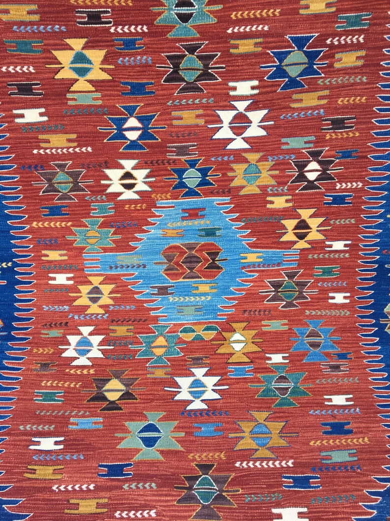 Puede incluir: Una alfombra roja, azul y blanca con dise&ntilde;os geom&eacute;tricos. La alfombra tiene un estilo tradicional y presenta una variedad de colores y formas.