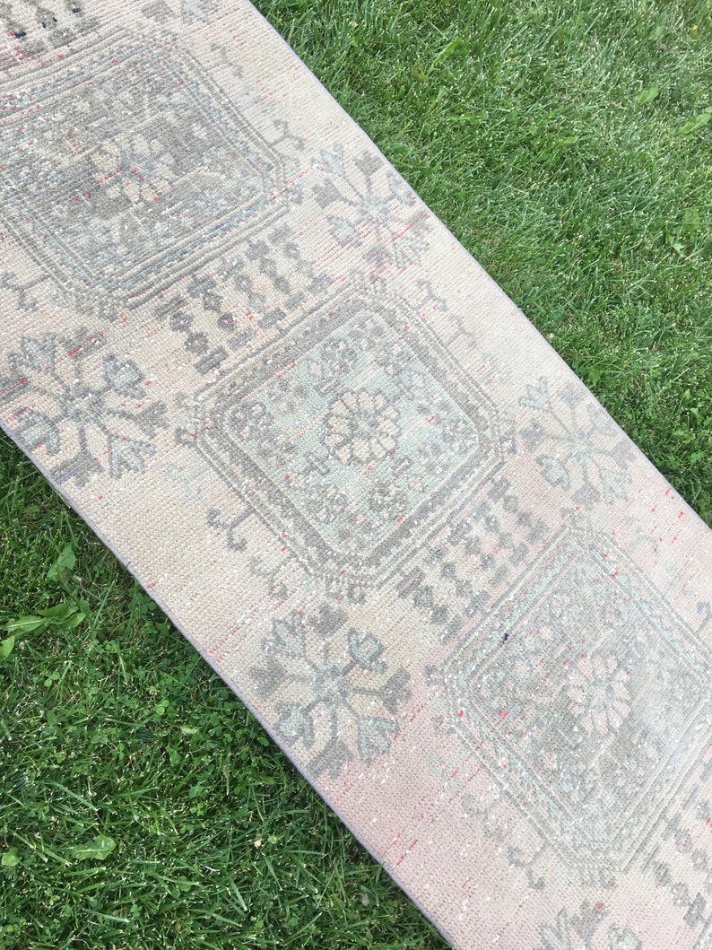 Op de afbeelding: Een lichtgrijze en roze loper met een traditioneel bloemenpatroon. De loper heeft een vervaagde, vintage uitstraling.