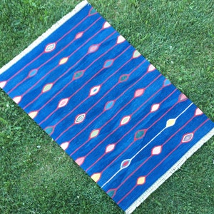 Puede incluir: Una alfombra azul con un patr&oacute;n repetitivo de l&iacute;neas rojas y dise&ntilde;os coloridos en forma de ojo.