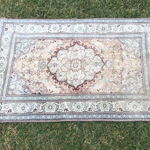 Peut inclure: Un tapis vintage avec un motif floral dans des tons beige, marron et bleu. Le tapis a un m&eacute;daillon central et une bordure aux motifs complexes.