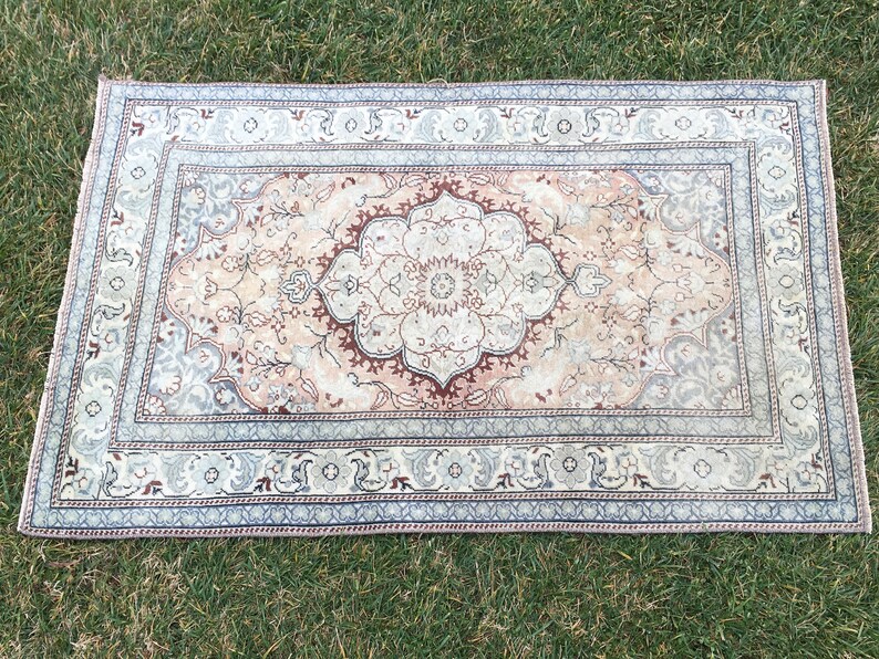 Peut inclure: Un tapis vintage avec un motif floral dans des tons beige, marron et bleu. Le tapis a un m&eacute;daillon central et une bordure aux motifs complexes.