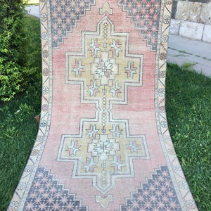 May include: A rectangular, vintage-style rug with a central geometric design in shades of peach, beige, and gold. The rug features a repeating pattern of floral and geometric shapes in the borders and corners, with accents of navy blue and gray. The rug is displayed outdoors on grass.
