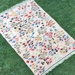 Puede incluir: Una alfombra rosa con un patr&oacute;n floral en tonos de azul, rojo, amarillo y verde. La alfombra tiene un borde de flecos.