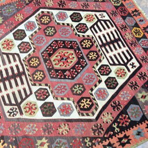 May include: A traditional Turkish rug with a geometric pattern in shades of red, black, white, and green. The rug features a central medallion with a repeating pattern of stars and diamonds.