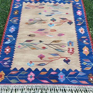 May include: A beige rug with a blue border and a floral pattern. The rug has a fringe on all sides.