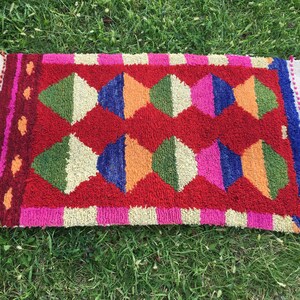 Puede incluir: Una alfombra colorida con un patr&oacute;n geom&eacute;trico de diamantes en tonos de rojo, verde, azul, naranja, rosa y blanco. La alfombra tiene un borde de flecos.