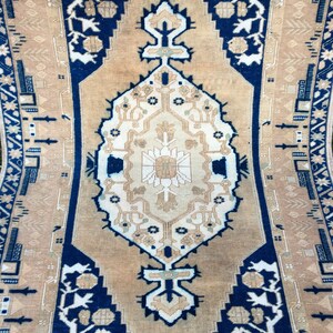 May include: A vintage rug with a beige background and a navy blue border. The rug features a central medallion with intricate floral patterns and geometric designs. The border is adorned with stylized floral motifs and geometric shapes.