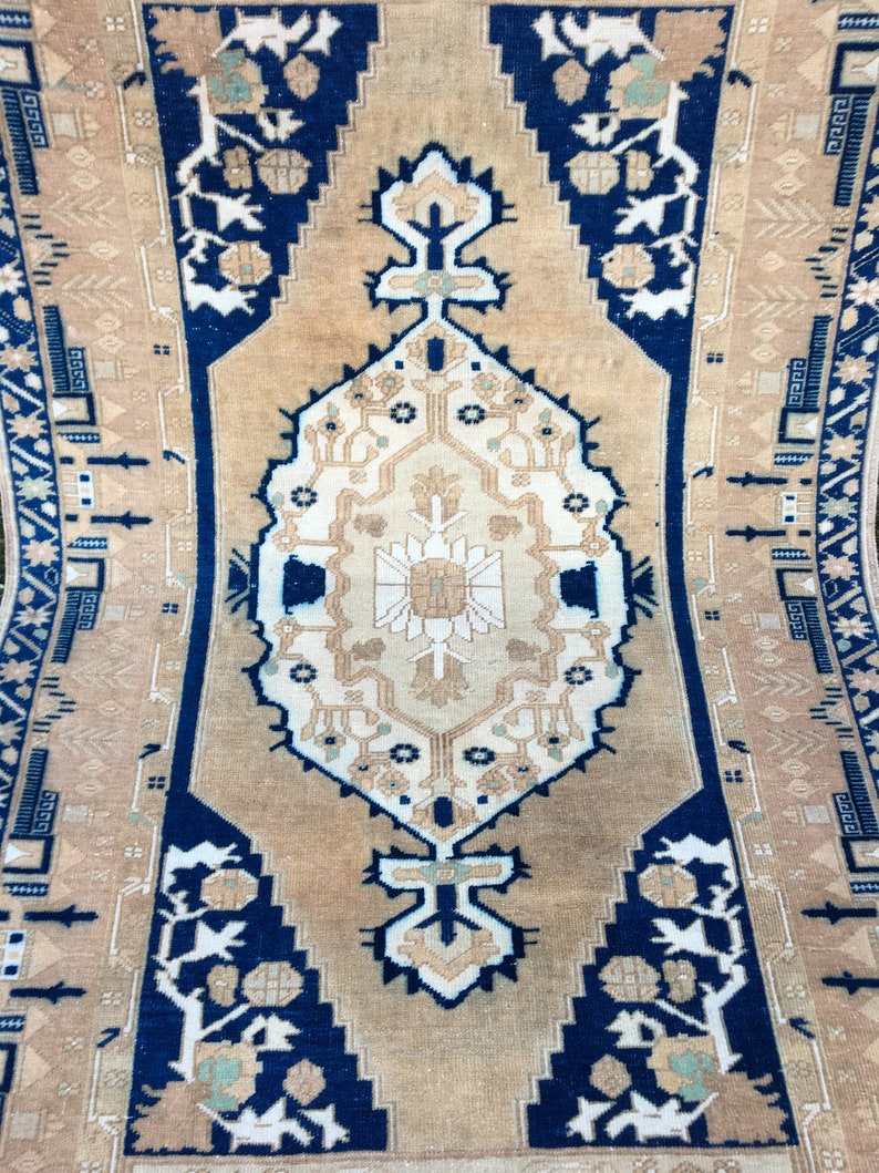 May include: A vintage rug with a beige background and a navy blue border. The rug features a central medallion with intricate floral patterns and geometric designs. The border is adorned with stylized floral motifs and geometric shapes.