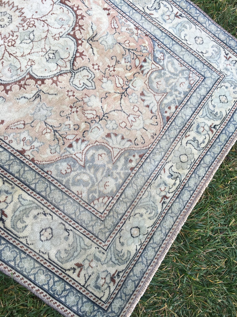 Peut inclure: Un tapis vintage de couleur bleu clair et beige. Le tapis pr&eacute;sente un motif floral avec un m&eacute;daillon central. Le tapis a une bordure &agrave; franges.