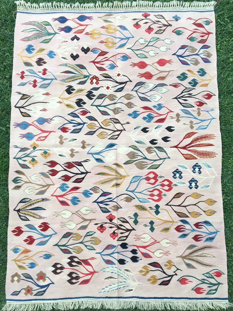 Puede incluir: Una alfombra rosa con un patr&oacute;n floral. La alfombra tiene un borde de flecos y presenta una variedad de colores, incluyendo rojo, azul, verde, amarillo y marr&oacute;n.