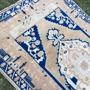 May include: A vintage rug with a blue and beige geometric pattern. The rug has a fringe border and is made of wool.