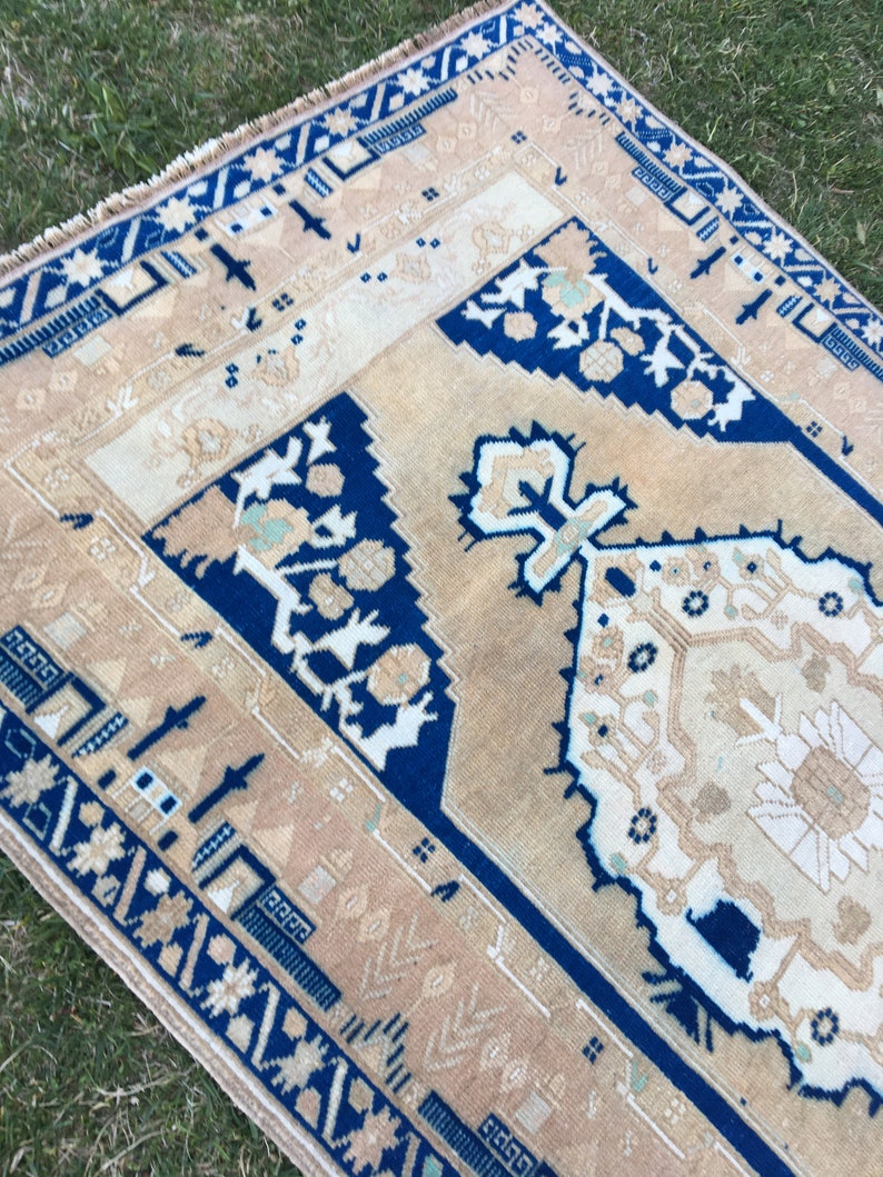 May include: A vintage rug with a blue and beige geometric pattern. The rug has a fringe border and is made of wool.
