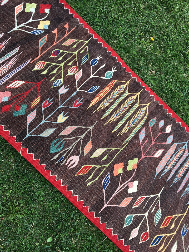 Puede incluir: Una alfombra de color marr&oacute;n y rojo con un dise&ntilde;o floral. La alfombra tiene un patr&oacute;n geom&eacute;trico con flores y hojas estilizadas en tonos de rojo, azul, amarillo, verde y rosa.