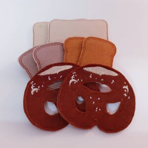 Puede incluir: Dos formas de pretzel de fieltro marr&oacute;n con bordados blancos, y tres formas de pan de fieltro beige, marr&oacute;n claro y marr&oacute;n oscuro.