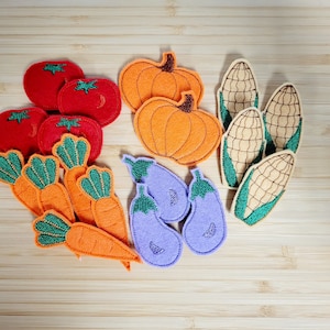 Puede incluir: Apliques de fieltro de varias verduras y frutas, incluyendo tomates rojos, calabazas naranjas, zanahorias verdes, berenjenas moradas y ma&iacute;z amarillo.
