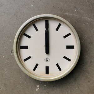 Può includere: Un quadrante di orologio bianco con lancette delle ore e dei minuti nere, indici orari romani neri e un logo a forma di diamante nero con le lettere "TN" all'interno. L'orologio ha una cornice in metallo argentato.