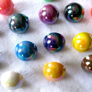 May include: A collection of iridescent glass marbles in various colours, including purple, blue, green, yellow, and orange. The marbles are arranged on a white surface.