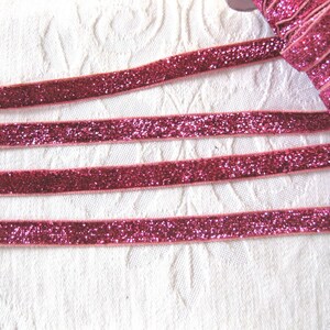 May include: Pink glitter ribbon with a velvet texture. The ribbon is shown in multiple strands on a white surface.