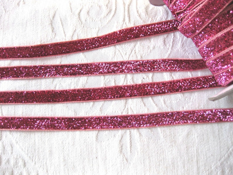 May include: Pink glitter ribbon with a velvet texture. The ribbon is shown in multiple strands on a white surface.