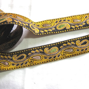 May include: Black and gold trim with paisley design. The trim has a black background with gold and silver thread embroidery. The trim is approximately 2.5 cm wide.