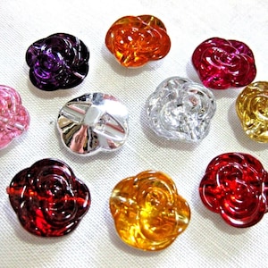 Könnte beinhalten: Sortiment aus zehn rosafarbenen Knöpfen aus Kunststoff in verschiedenen Farben, darunter rosa, lila, rot, orange und silber.