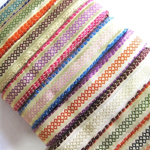 May include: A stack of colourful striped ribbon trim with a diamond pattern. The ribbon is beige with a variety of coloured stripes, including green, orange, red, purple, blue, and pink.