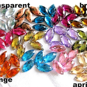 Könnte beinhalten: Sortiment an bunten, facettierten, marquiseförmigen Glas-Strasssteinen. Die Farben umfassen transparent, orange, braun, aprikose, rosa, lila, blau und grün.