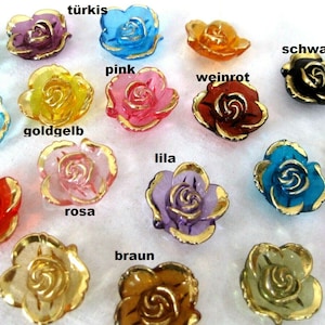 Könnte beinhalten: Sortiment von 14 rosenförmigen Glasknöpfen mit goldener Einfassung in verschiedenen Farben, darunter Rot, Rosa, Gold, Türkis, Braun, Lila und Schwarz. Die Knöpfe sind in einem Halbkreis auf einer weißen Oberfläche angeordnet.