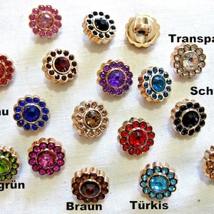 May include: Assortment of 15 gold-tone metal buttons with various colored rhinestones. The buttons feature a flower-shaped design with a single rhinestone in the center. The colors include red, blue, green, purple, pink, brown, turquoise, black, and clear.