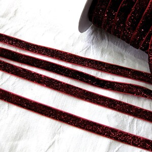 May include: Red velvet ribbon with glitter, shown in multiple strands on a white surface.