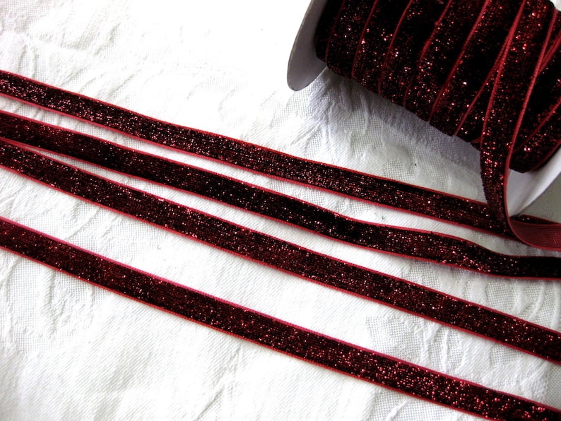 May include: Red velvet ribbon with glitter, shown in multiple strands on a white surface.