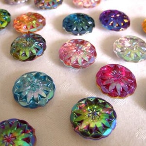 Könnte beinhalten: Sortiment an regenbogenfarbenen Glasknöpfen in verschiedenen Farben, darunter Rosa, Blau, Grün und Lila. Die Knöpfe haben ein blumenartiges Design und sind perfekt für Bastelprojekte.
