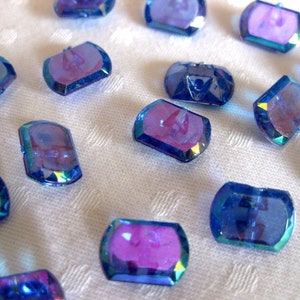 May include: Assortment of iridescent blue and purple faceted glass buttons. The buttons are shaped like elongated ovals with rounded edges.