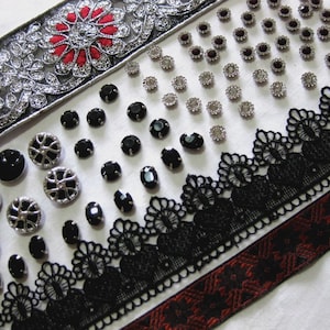May include: An assortment of decorative embellishments, including black and silver buttons, black lace trim, and red and silver embroidered ribbon. Various sizes and shapes of embellishments are displayed on a white surface.