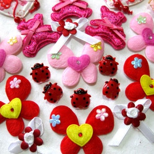 Op de afbeelding: Assortiment van vilt handwerkversieringen in roze, rood en geel. De versieringen omvatten vlinders, lieveheersbeestjes, bloemen en harten.