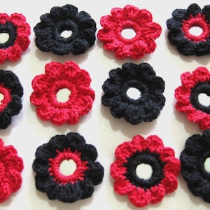 Puede incluir: Primer plano de flores de ganchillo hechas a mano. Las flores alternan entre pétalos rojos con centro negro y pétalos negros con centro rojo. Cada flor tiene un centro blanco.