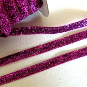 May include: Pink glitter ribbon with a velvet texture. The ribbon is rolled up and there are two strands of ribbon laid out flat.