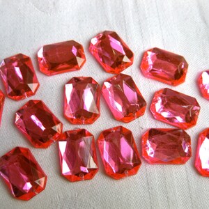 May include: A collection of 15 pink plastic faceted gems in a rectangular shape.