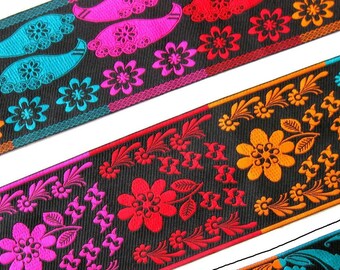 Op de afbeelding: Een close-up van een kleurrijk lint met een zwarte achtergrond en bloemmotieven. Het lint heeft een verscheidenheid aan kleuren, waaronder oranje, roze, rood en blauw.