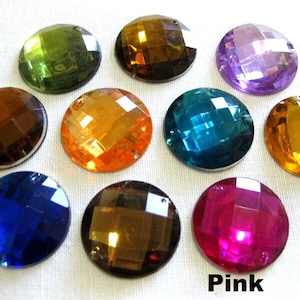 Könnte beinhalten: Sortiment aus zehn runden, facettierten, irisierenden Glas-Steinen in verschiedenen Farben, darunter Grün, Braun, Lila, Orange, Blau und Pink. Die Steine sind in einem Kreis auf einer weißen Oberfläche angeordnet.