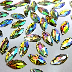 Może przedstawiać: Kolekcja tęczowych, markizowych cyrkonii z efektem tęczy. Cyrkonie mają płaską tylną stronę i dwa otwory do szycia lub mocowania.