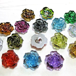 Op de afbeelding: Assortiment van 15 metalen roosvormige knopen in verschillende kleuren, waaronder zilver, goud, groen, blauw, paars, rood en bruin.