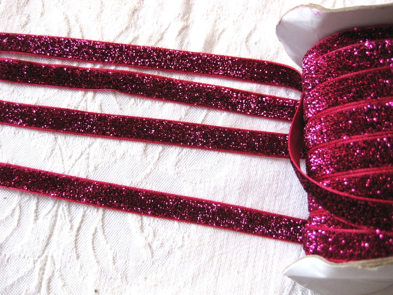 May include: A spool of pink glitter ribbon. The ribbon is rolled up and has a white label.