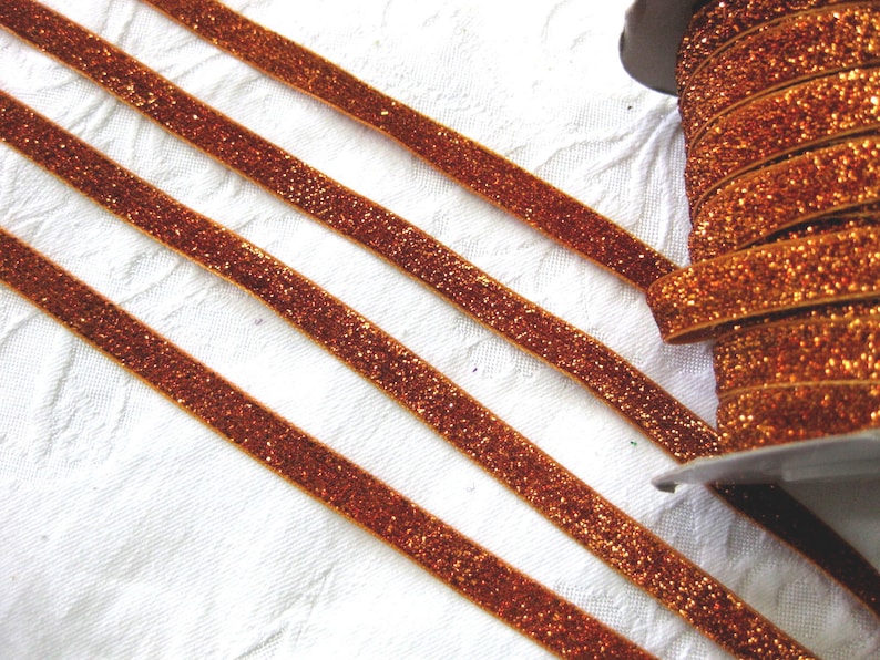 May include: A spool of orange glitter ribbon. The ribbon is a thin, flat strip with a sparkly finish.