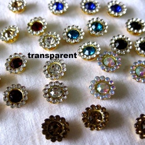 May include: Assortment of small, round, decorative embellishments with rhinestones in various colours, including clear, blue, red, and iridescent. The embellishments are set in gold-toned metal.