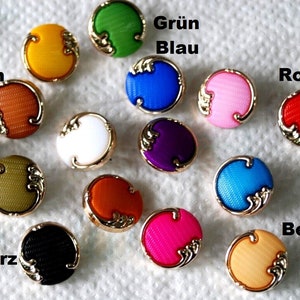 Könnte beinhalten: Sortiment von 14 runden Knöpfen in verschiedenen Farben, darunter Rot, Blau, Grün, Gelb, Orange, Braun, Schwarz, Weiß, Lila, Rosa, Beige und Türkis. Jeder Knopf hat einen goldfarbenen Rand und ein dekoratives Design.