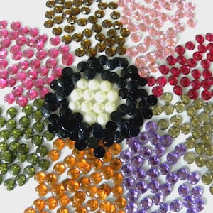 Può includere: Vista dall'alto di una composizione floreale di perline sfaccettate multicolori. Le perline sono rosa, marroni, nere, bianche, verdi, arancioni, viola e rosse. Le perline sembrano essere di vetro o cristallo.