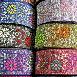 May include: A stack of colourful embroidered trim with floral patterns in shades of pink, green, blue, orange, and purple. The trim is on a white background.