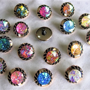 Peut inclure: Assortiment de 15 boutons irisés avec une bordure dorée et des accents noirs. Les boutons sont de différentes couleurs, notamment rose, bleu, vert et orange.