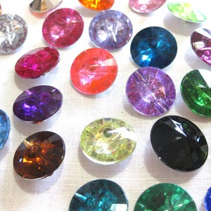 May include: Assortment of colorful, round, faceted glass buttons. The buttons are various colors, including red, blue, green, purple, orange, and black.
